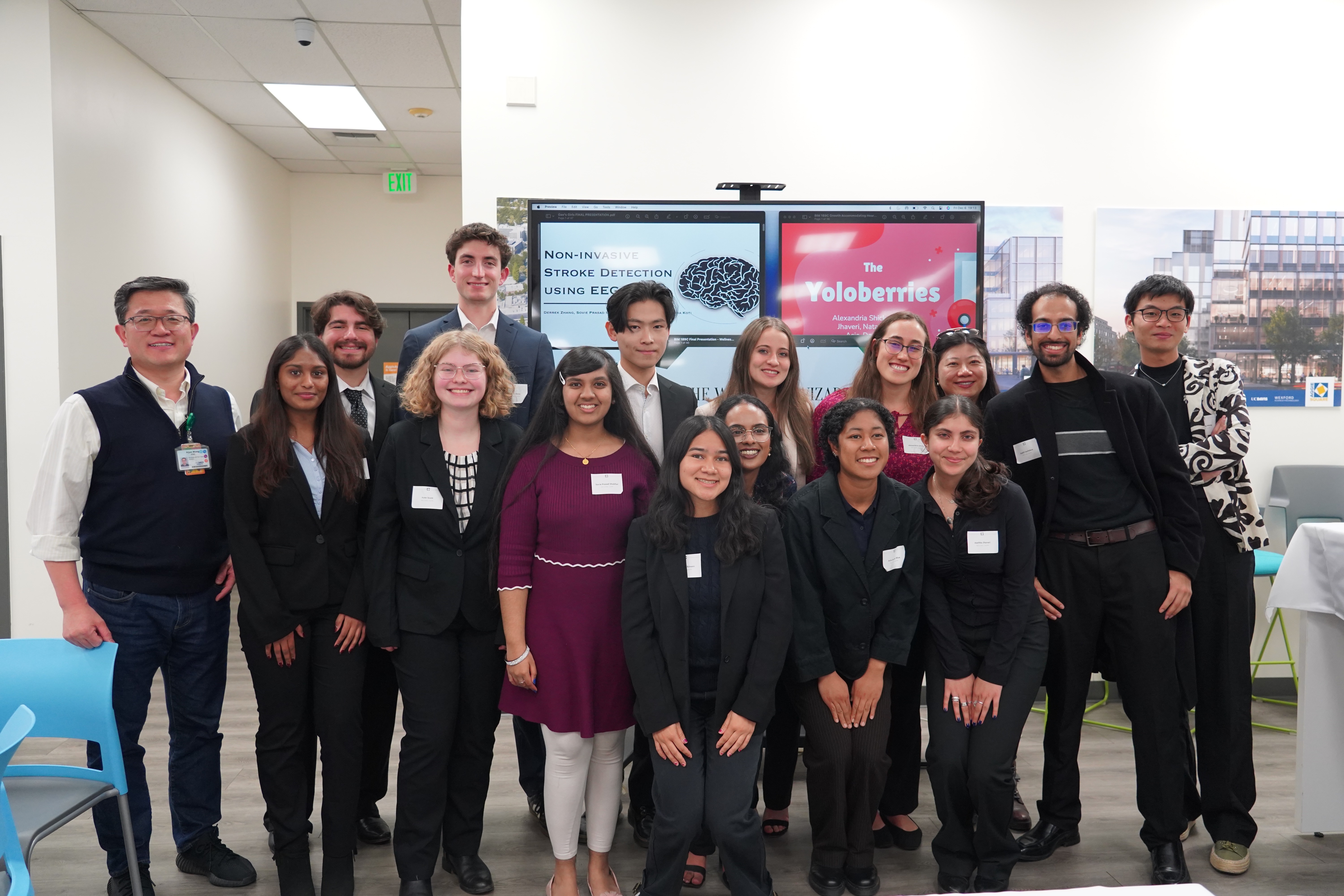 large group of students and faculty standing in front of a screen with images from the presentations on the screen.