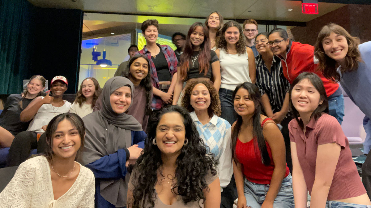 A group of smiling students pose together for a photo inside Aggie Square