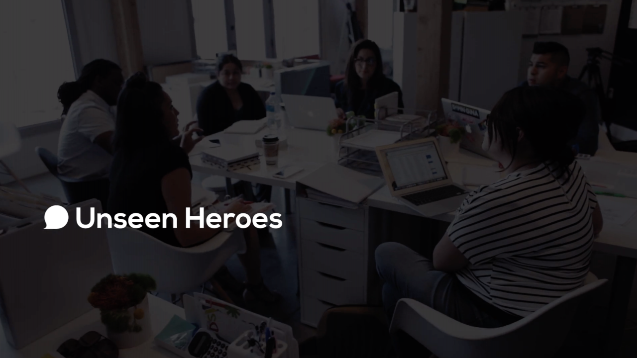 Unseen Heroes Promotional Video thumbnail. Translucent black screen with "UNSEEN HEROES" text overlaid on image of their team working around a  table