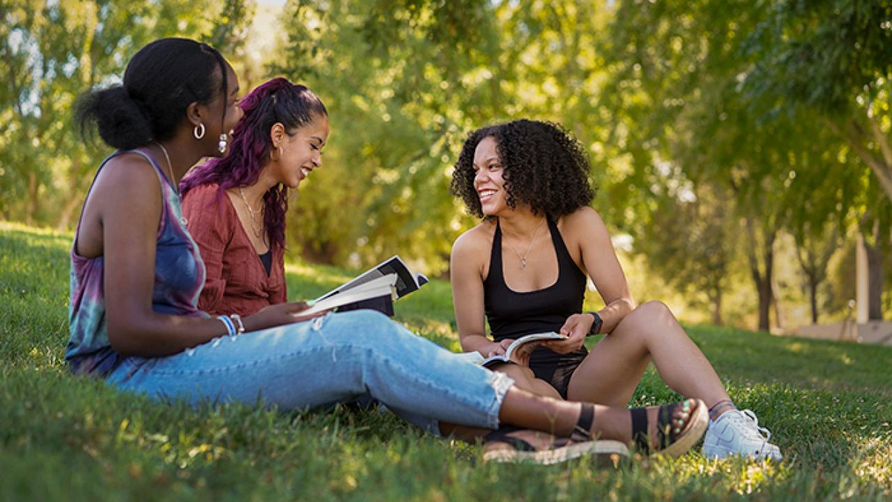 Kyerah Kyles, Andrea Medina and Laurenne Sanchez sitting in the grass with books
