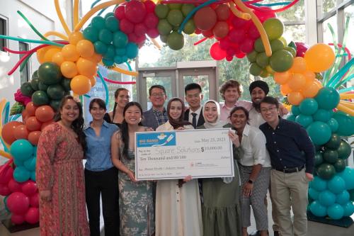 Group of 10 students display large $10,000 check while posing under a colorful balloon arch. 