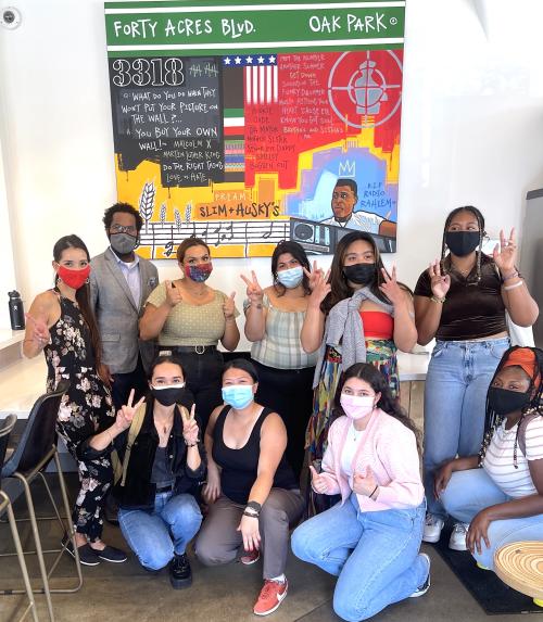 A group of Transformative Justice Studies students in front of a vibrant mural at Slim and Husky's