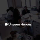Unseen Heroes Promotional Video thumbnail. Translucent black screen with "UNSEEN HEROES" text overlaid on image of their team working around a  table